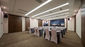 Un salón de conferencias con mesas dispuestas para una reunión, una pantalla grande mostrando una presentación y una puerta a la izquierda.