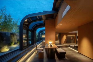 Un interior moderno con una pared curva de vidrio, una zona de estar con mesa y sillas, y un revestimiento de madera.