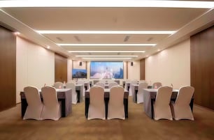 A conference room with tables and chairs, a large window with a cityscape view, and recessed lighting.