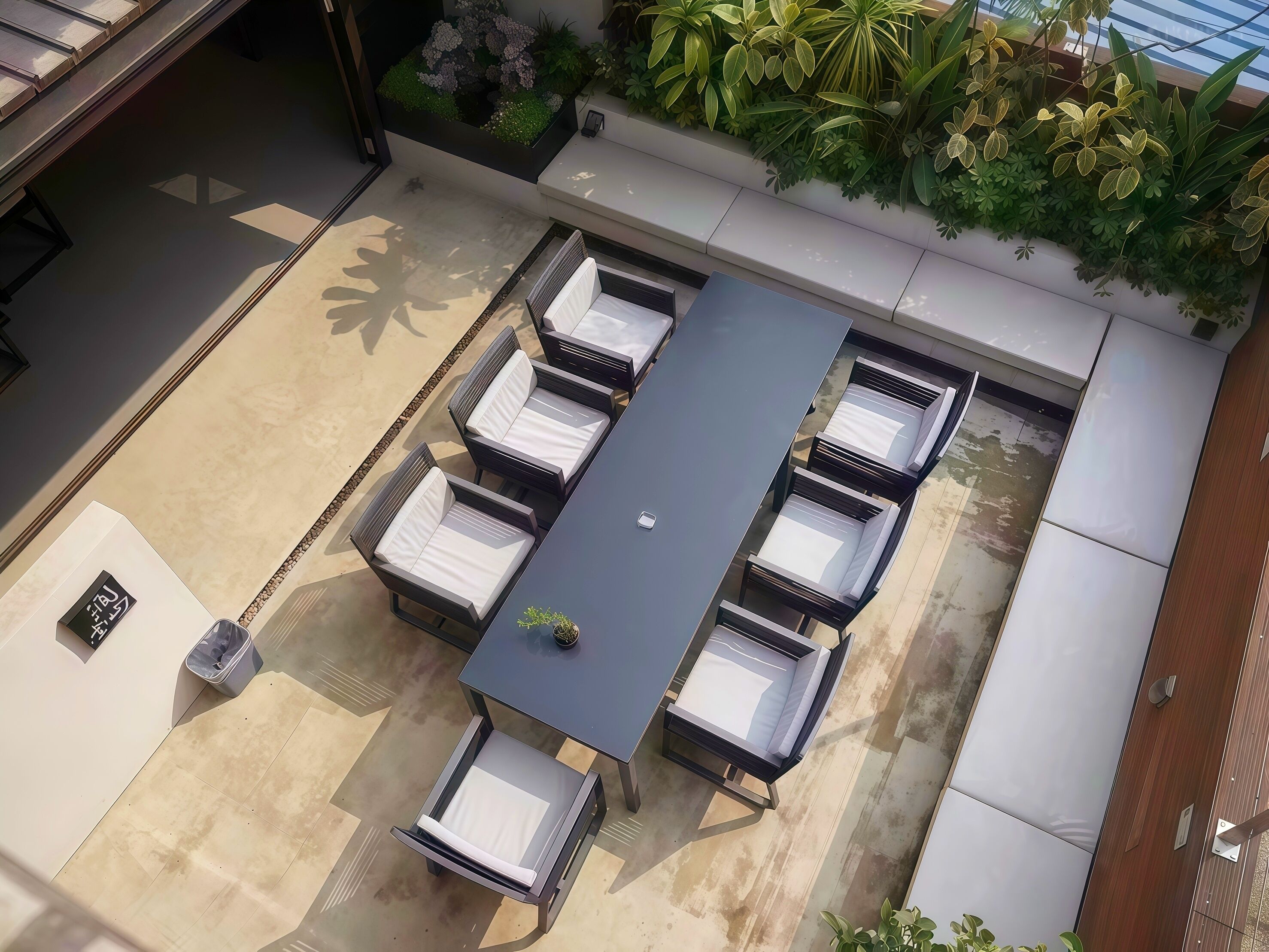 Una terraza en la azotea con una mesa larga y seis sillas, rodeada de vegetación y un edificio moderno.