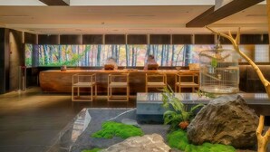 Un moderno vestíbulo de hotel con mostrador de recepción, zona de estar y un amplio ventanal con vista a un bosque.