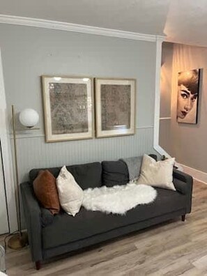 A living room with a grey sofa, framed artwork on the wall, and a floor lamp. - Clinton St Townhouse (Lafayette)