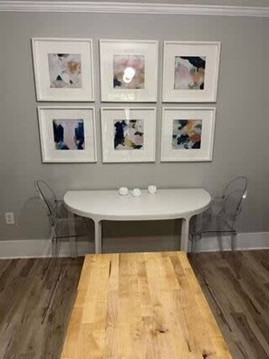 A dining area with a wooden table and six framed abstract artworks on the wall. - Clinton St Townhouse (Lafayette)