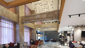 A spacious lobby with high ceilings, a chandelier, seating areas, and a bookshelf. - Campanile Hotel (Huaibei)