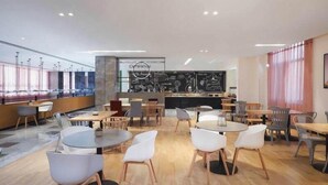 A modern hotel lobby with round tables and chairs, a reception desk, and a large window with curtains. - Campanile Hotel (Huaibei)