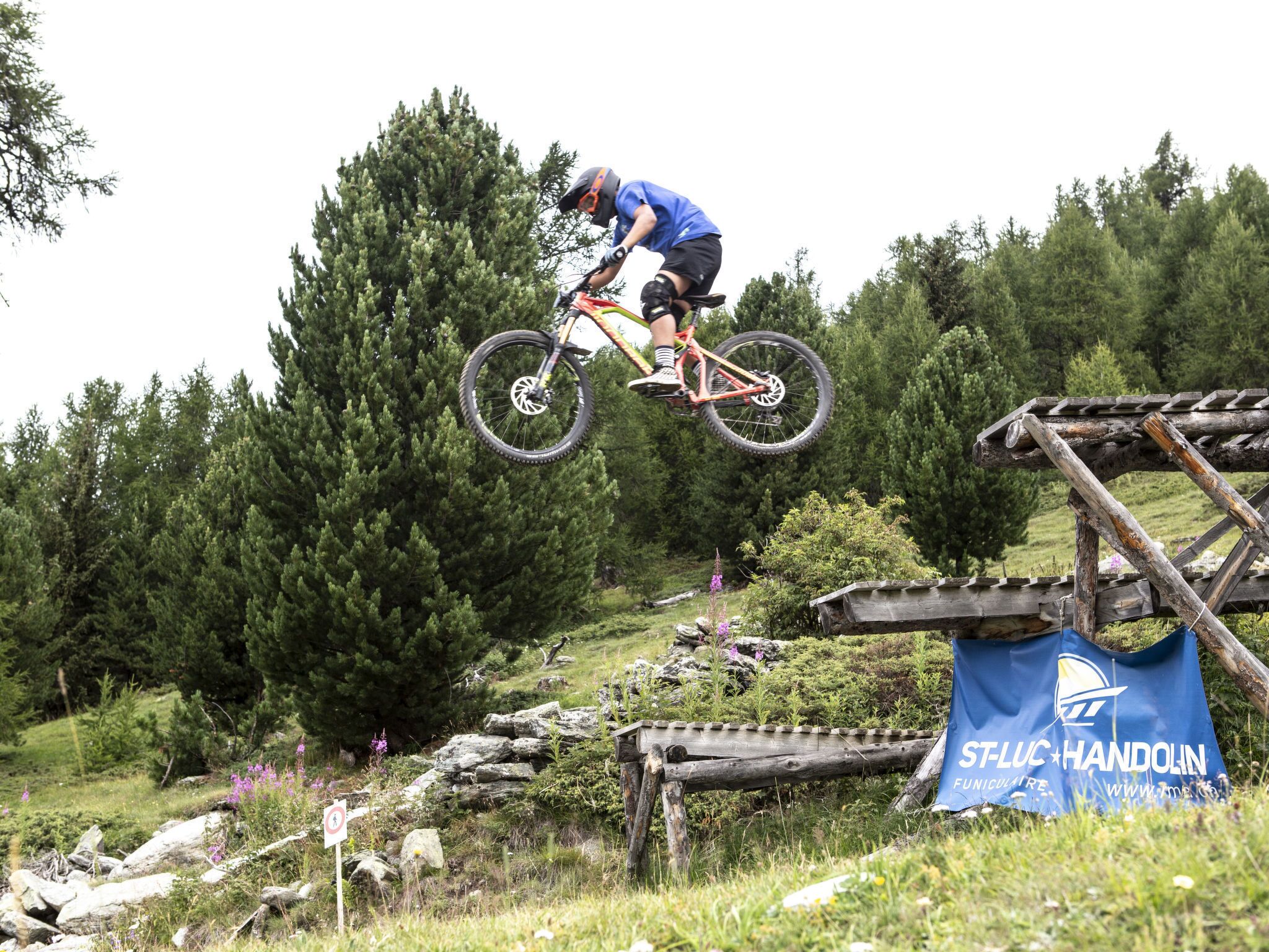 A mountain biking event with a wooden obstacle course and a sign for 'ST-LUC HANDOLIN FUNICULATRE.'