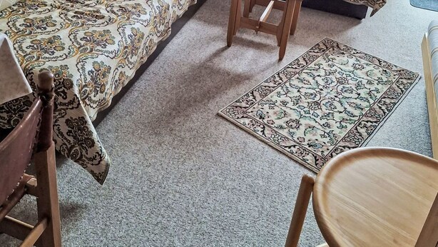 Een woonkamer met een zithoek, een klein houten tafeltje en een kamerkleed met een patroon.