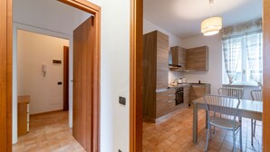 A modern kitchen with wooden cabinets, a dining area with metal chairs, and a hallway with a wooden door. - Manzoni 2 - Beyond the Duomo (Como)