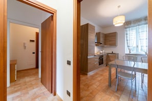 Eine moderne Küche mit Holzschränken, ein Essbereich mit Metallstühlen und ein Flur mit einer Holztür.