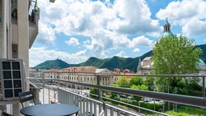 A balcony with a table and chairs, overlooking a street with cars and buildings, including a church with a green dome. - Manzoni 2 - Beyond the Duomo (Como)