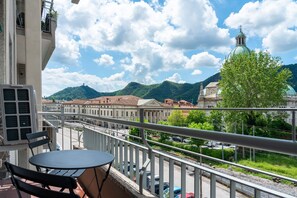 Ein Balkon mit Tisch und Stühlen, der auf eine Straße mit Autos und Gebäuden blickt, darunter eine Kirche mit einer grünen Kuppel.