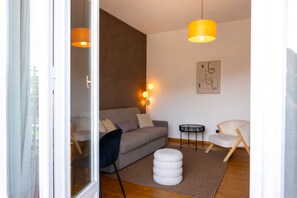 Ein modernes Wohnzimmer mit einer Couch, einem runden Hocker, einem Sessel, einem kleinen Tisch und einer Wandlampe.