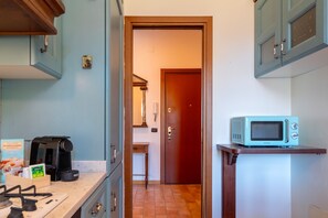 A kitchen with a microwave on a shelf, a coffee maker, and a door leading to another room. - Manzoni 2 - Dome View Apartment (Como)