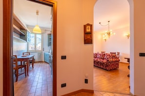 Ein Flur, der in einen Essbereich mit einem Holztisch und Stühlen, einem roten, gemusterten Sofa und einer Kandelaber führt.