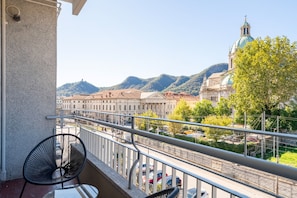 Ein Balkon mit Stuhl, Tisch und Blick auf eine Stadtlandschaft mit einem markanten Gebäude und Bergen.