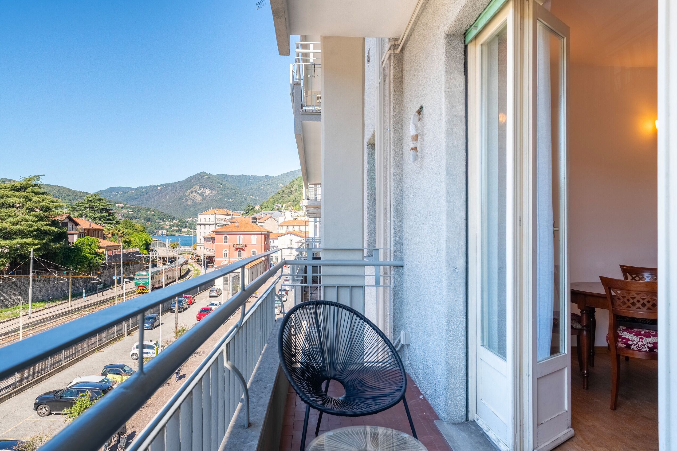 A balcony with a view of a street and mountains, a chair, and a table with chairs.