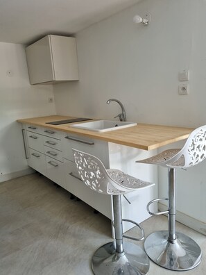 Eine kleine Küchenzeile mit Spüle, Holzausziehtisch und zwei Stühlen mit Metallbeinen.