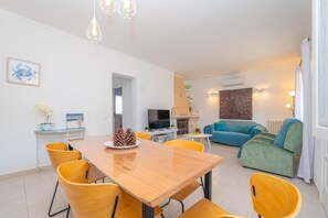A modern living room with a blue sofa, a dining area with yellow chairs, and a kitchen area with a TV and oven. - CAN PARÍS – Beautiful house just two minutes from the beach with free Wi-Fi (Santa Margalida)