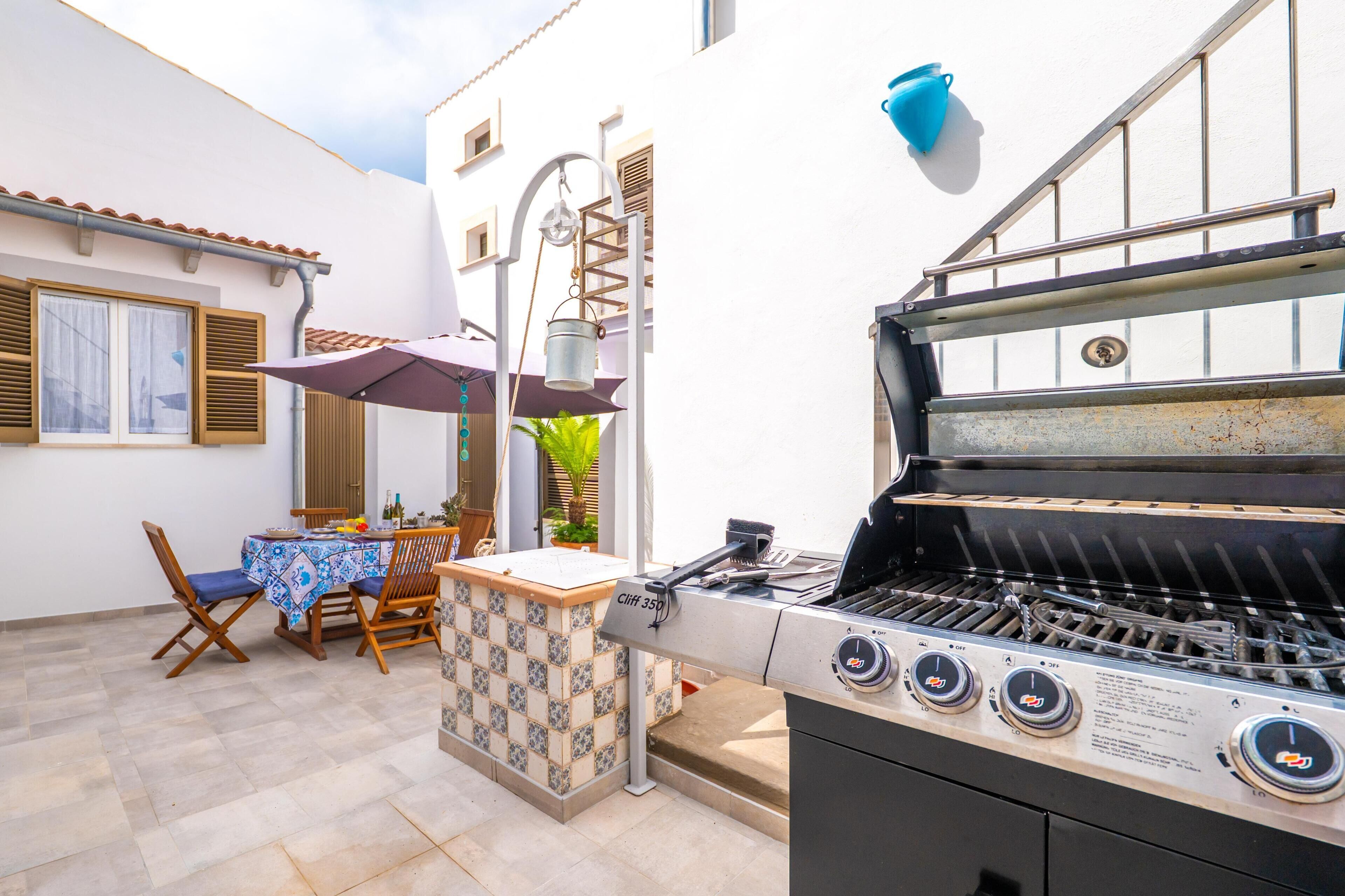 An outdoor patio with a barbecue grill, a table with chairs, and a hanging light fixture.