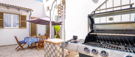 Un patio al aire libre con una parrilla, una mesa con sillas y una lámpara colgante.
