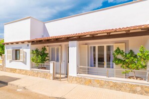 A two-story building with a white facade, red-tiled roof, and a stone base. There are two balconies with metal railings and potted plants. - CAN PARÍS – Beautiful house just two minutes from the beach with free Wi-Fi (Santa Margalida)