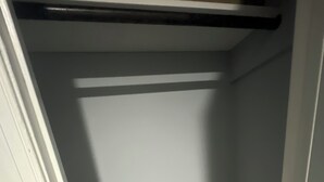 A closet with a hanging rod, a door, and a corner with a shadow.