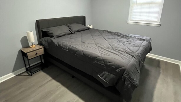 Ein Schlafzimmer mit Bett, Nachttisch, Fenster und Deckenleuchte.