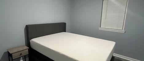 A bedroom with a single bed, a nightstand, a window with blinds, and a ceiling light.