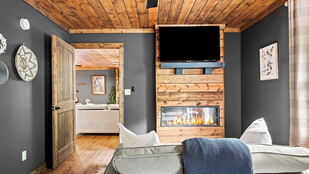 A living room with a fireplace, a television mounted on a wooden wall, and a sofa. - 3 King Suites, Game Room, Hot Tub - 2 Mi to Island (Pigeon Forge)