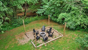 An outdoor seating area with a fire pit and chairs arranged around it, surrounded by a wooden fence and lush greenery. - 3 King Suites, Game Room, Hot Tub - 2 Mi to Island (Pigeon Forge)