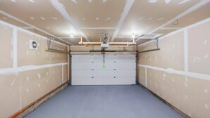 Ett garage med en stängd garagedörr, en takfläkt och infälld belysning.