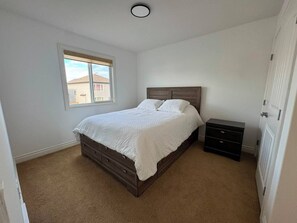 A bedroom with a bed, a nightstand, a dresser, and a window. - Modern Windermere Home | Sleeps 6 | Near Shopping & Airport (Edmonton)