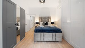 A bedroom with a bed, bedside tables, a wardrobe, and a mirror. - Superior Bedroom Apartment In Mayfair (London)