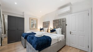 A bedroom with two beds, a grey headboard, a mirror, and a wardrobe. - Superior Bedroom Apartment In Mayfair (London)