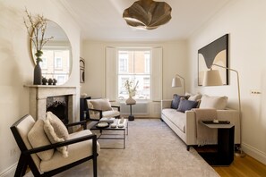 A living room with a fireplace, a sofa, a coffee table, and a lamp. - Luxury 3 Bedroom Kensington Townhouse With Private Garden (London)