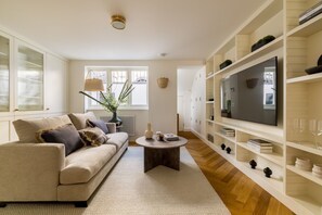 A modern living room with a sofa, coffee table, TV, and built-in shelving. - Luxury 3 Bedroom Kensington Townhouse With Private Garden (London)
