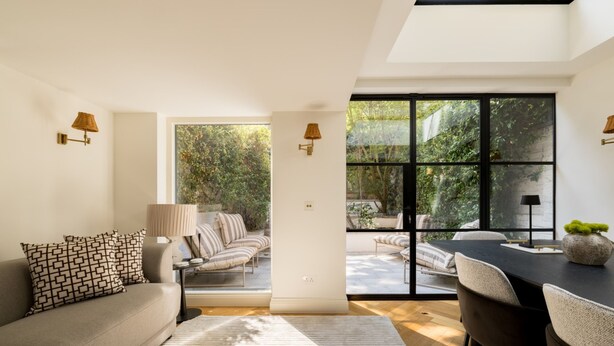 Ein modernes Wohnzimmer mit einer Couch, einem Esstisch und Blick ins Freie durch große Fenster.