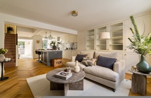 A spacious living room with a sofa, coffee table, and a view into the kitchen. - Luxury 3 Bedroom Kensington Townhouse With Private Garden (London)