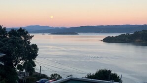 Un plan d’eau paisible, avec un coucher de soleil en arrière-plan, entouré de collines et d’arbres.