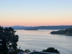 Ruhige Wasserfläche, im Hintergrund ein Sonnenuntergang, umgeben von Hügeln und Bäumen.