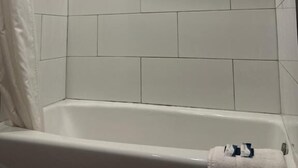 Et hjørnebadeværelse med hvide fliser, et badekar og en håndklædestang.