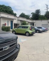 Un estacionamiento con varios autos, incluyendo un hatchback verde y un SUV negro.