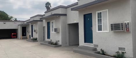 A row of single-story buildings with individual garage doors, small steps leading to the entrances, and air conditioning units mounted on the walls.