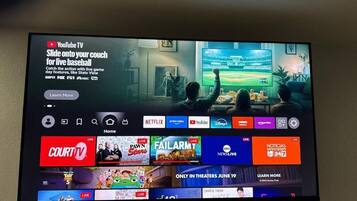 Uma televisão exibindo a interface do YouTube TV com diversos canais de TV ao vivo e uma partida de beisebol em andamento.