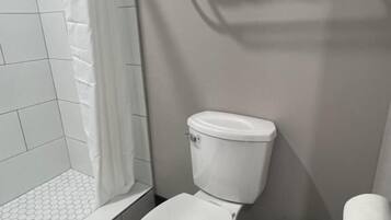 Un baño con inodoro blanco, zona de ducha y un perchero para toallas.