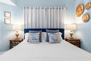Ein Schlafzimmer mit einem Bett, zwei Nachttischen, einer Kopfteil und einer Wand mit Dekoration.