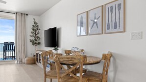 Zona pranzo con un tavolo rotondo in legno, quattro sedie in legno, una TV a schermo piatto montata a parete e tre opere d'arte a tema nautico.