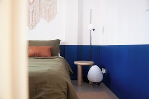 A bedroom with a bed, a bedside table, a lamp, and a wall-mounted macrame decoration. - Flinder's Keepers | Artist's Retreat | 3BR+Parking (Melbourne)