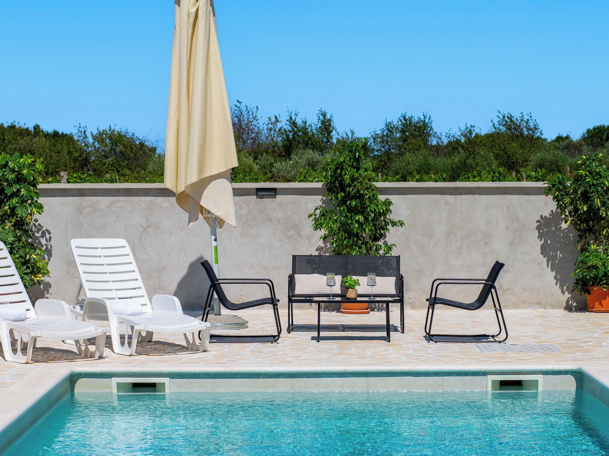 A poolside area with lounge chairs, a table with drinks, and a large umbrella.
