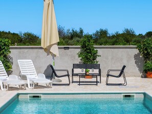 Ein Poolbereich mit Liegestühlen, einem Tisch mit Getränken und einem großen Sonnenschirm.